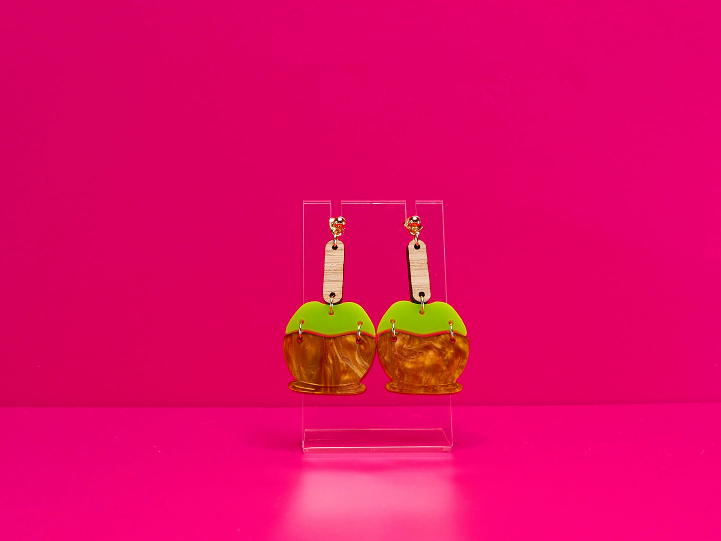 Earrings on a clear display against a hot pink background.