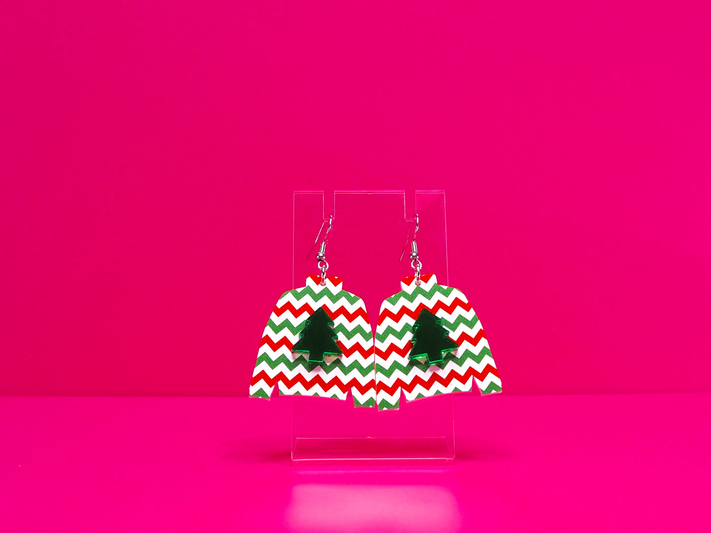 Earrings on a clear display against a hot pink background.