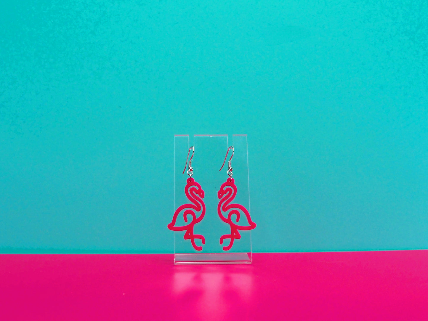 Hot pink flamingo earrings against a blue and pink background.