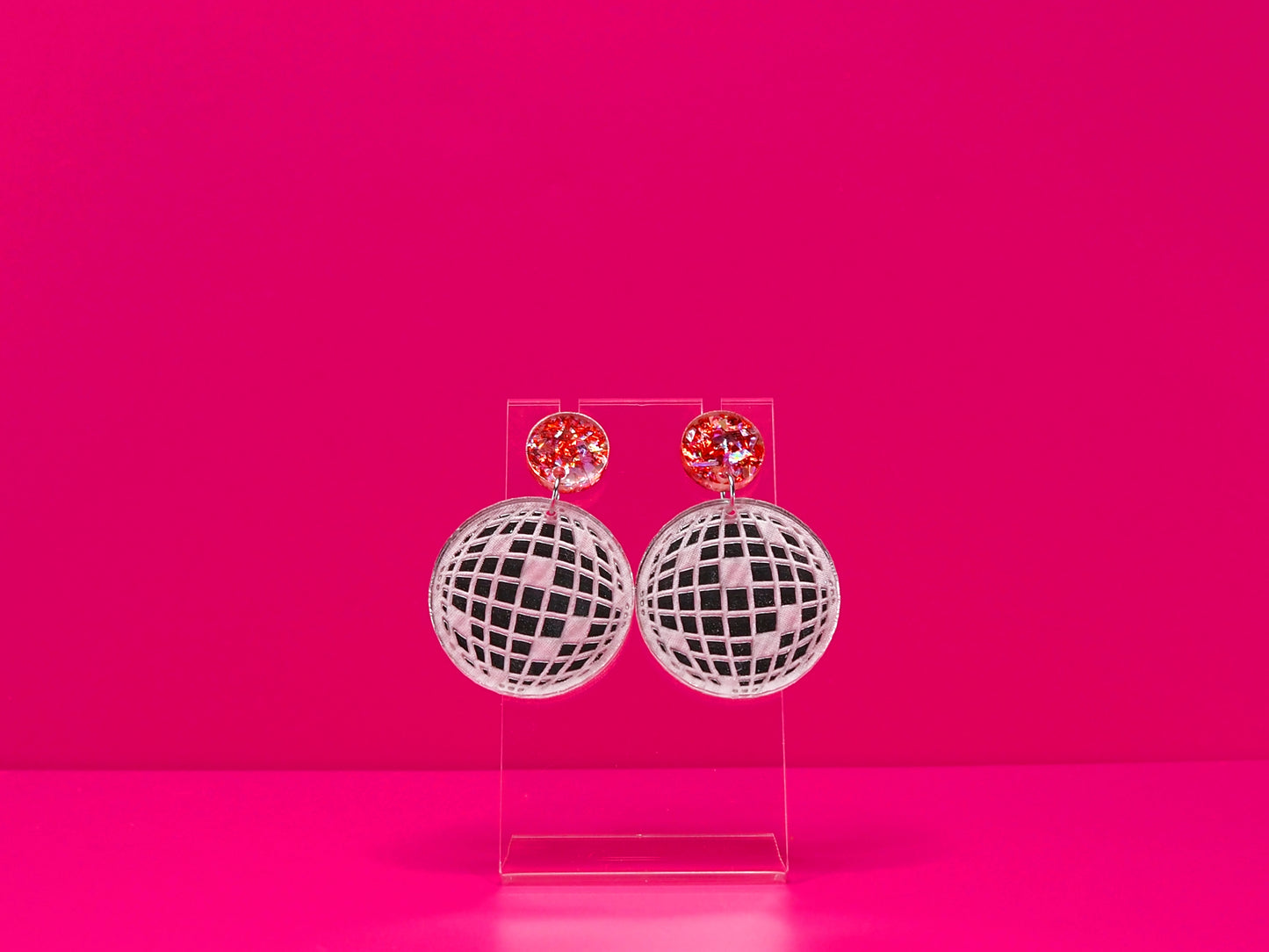 Flat disco ball earrings with a metallic pink topper against a hot pink background.