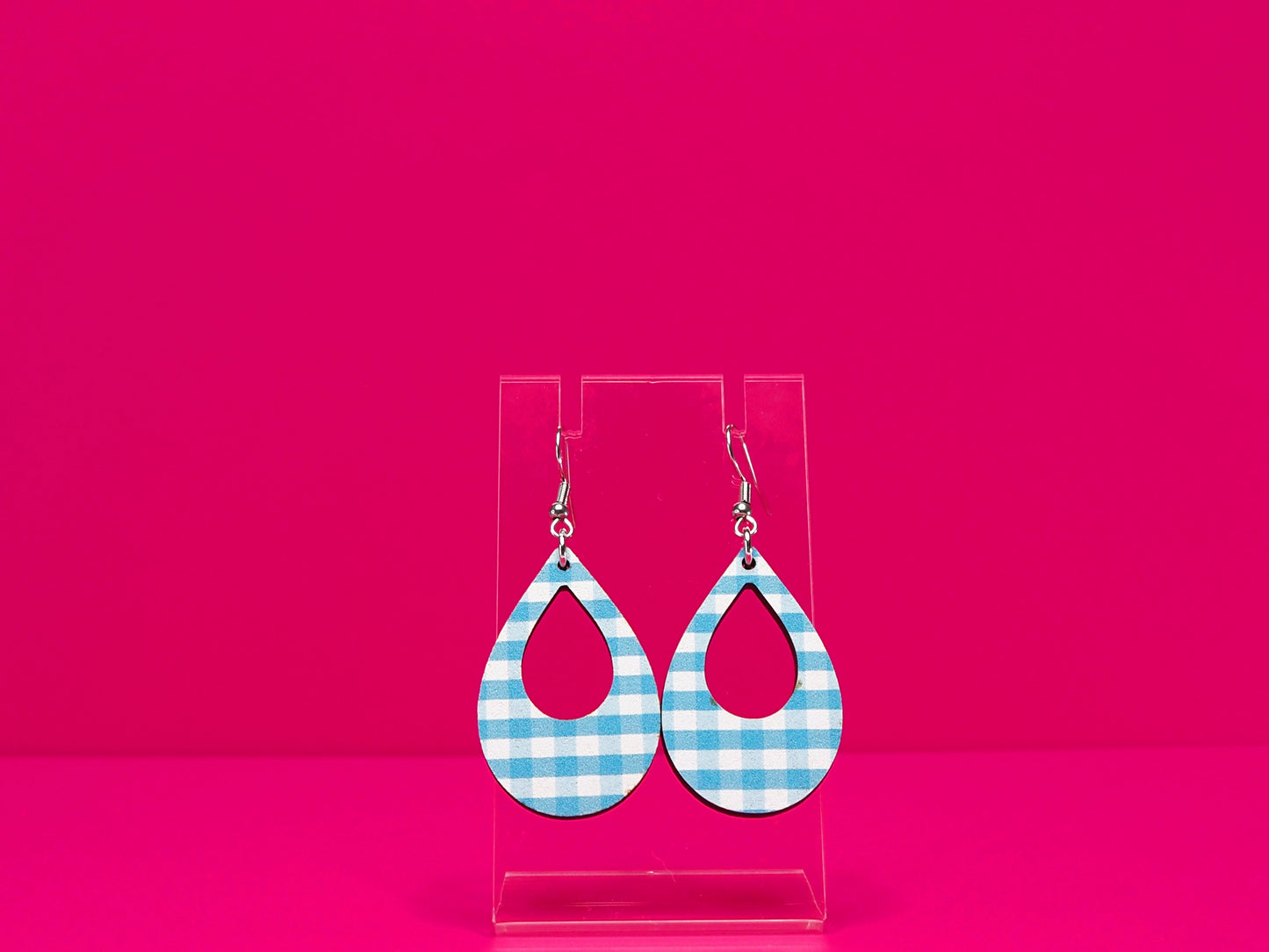 Light blue gingham tear drop shaped earrings on a clear display against a hot pink background.