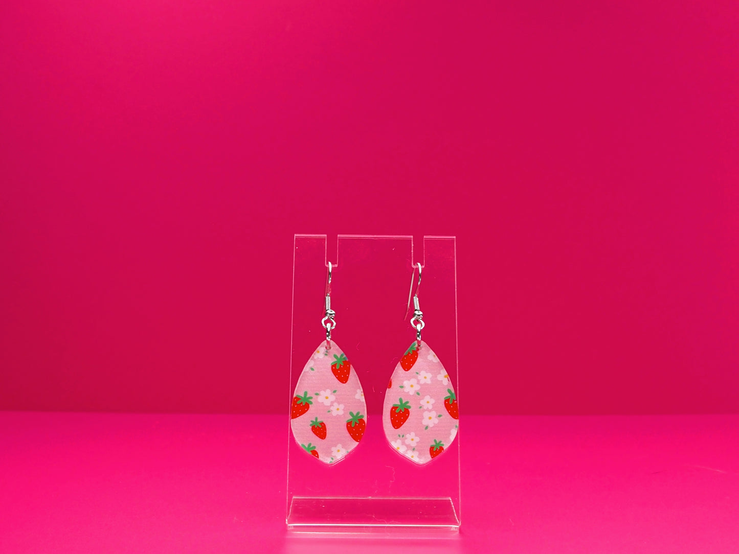 Strawberry Delight earrings on a clear display against a pink background.