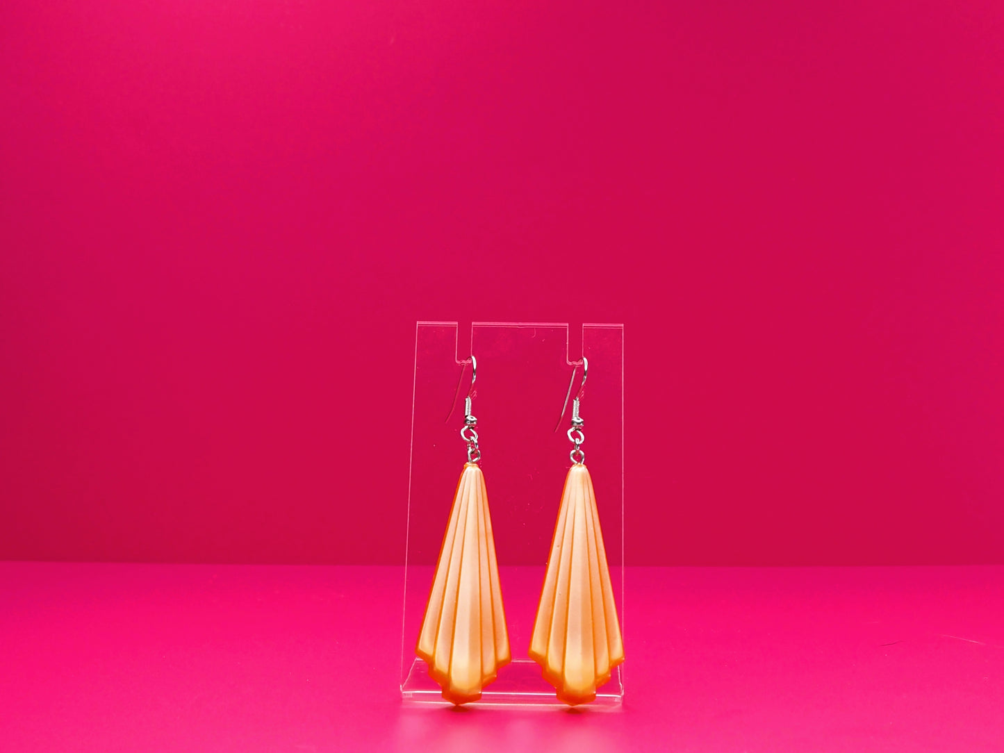 Art deco earrings on a clear display against a pink background.