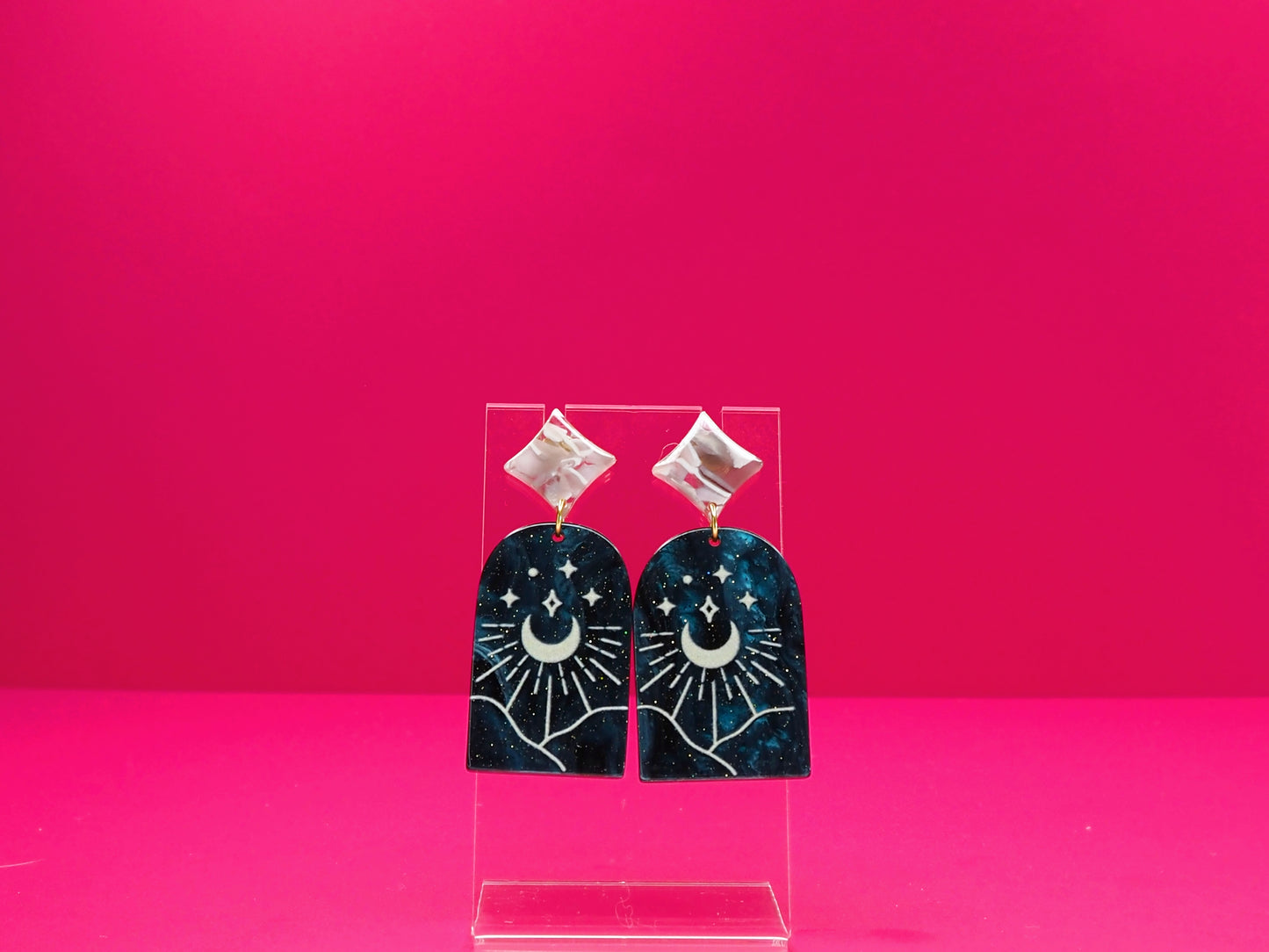 Star and moon arch earrings on a clear display against a pink background.