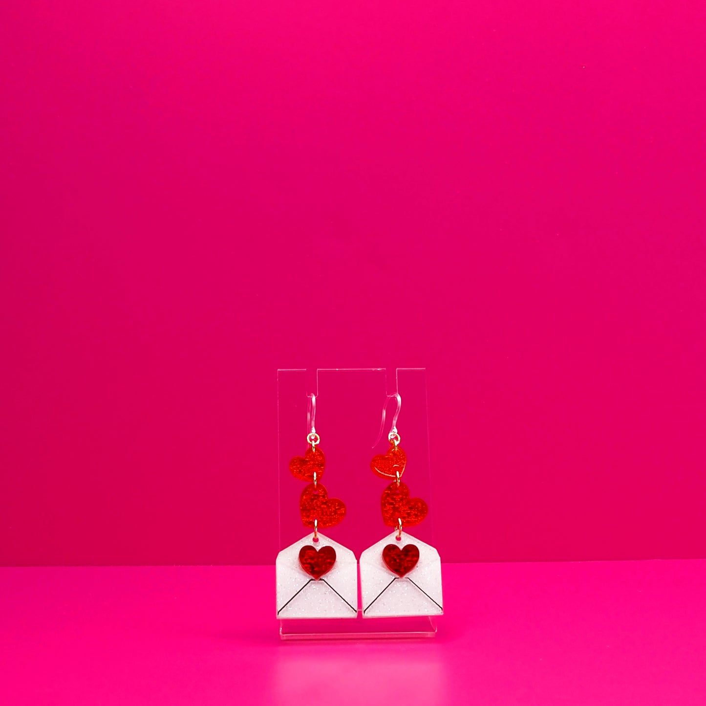 Red hearts cascading into a white envelope on a clear stand against a pink background.