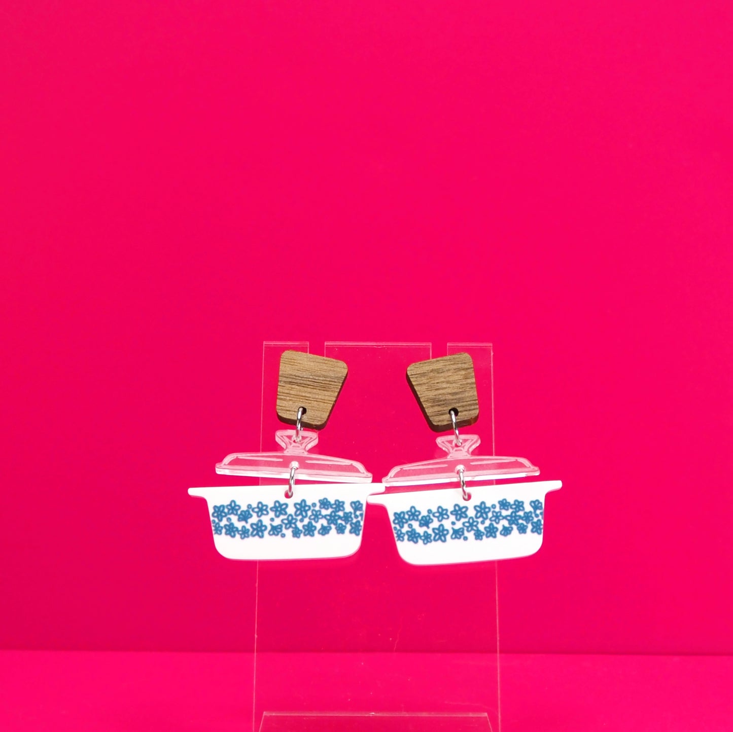 Vintage casserole dish in white earrings with wood accents on a clear display against a pink background.