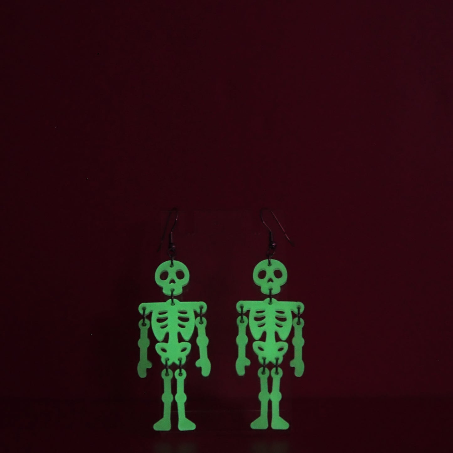 Dangling skeleton earrings shown glowing green against a dark background.