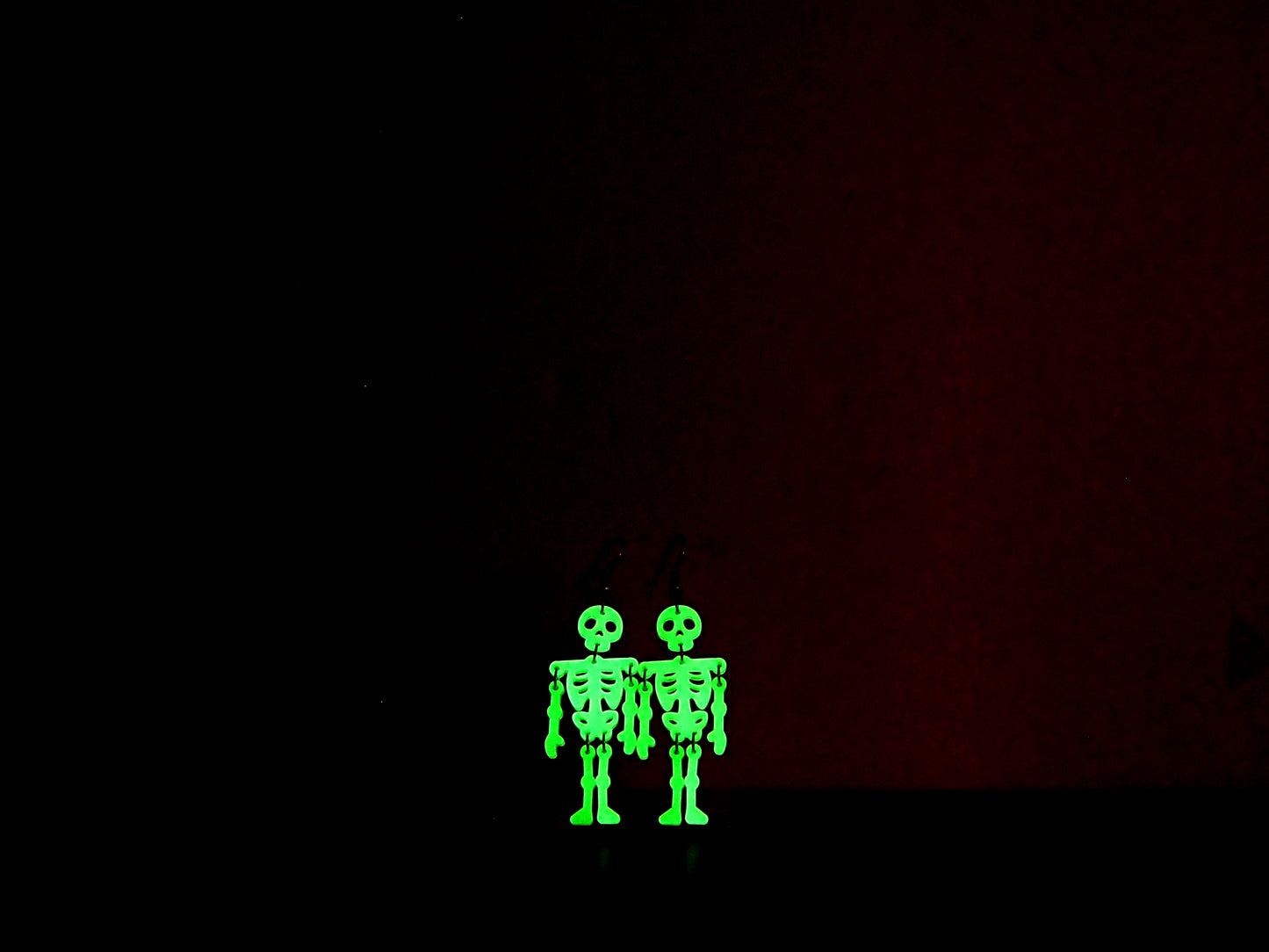 Skeleton earrings in the dark to show their green glow against a dark background.