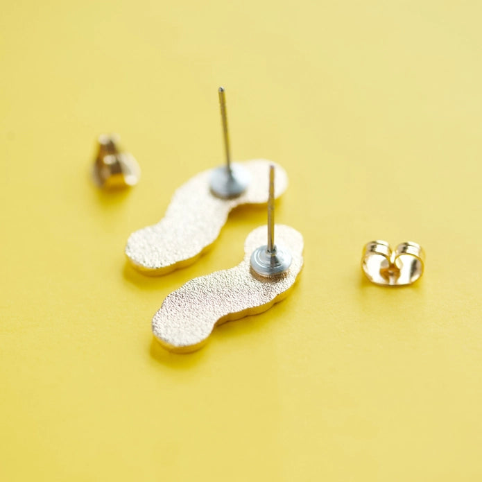 Gummy worm earrings face down against a yellow background.