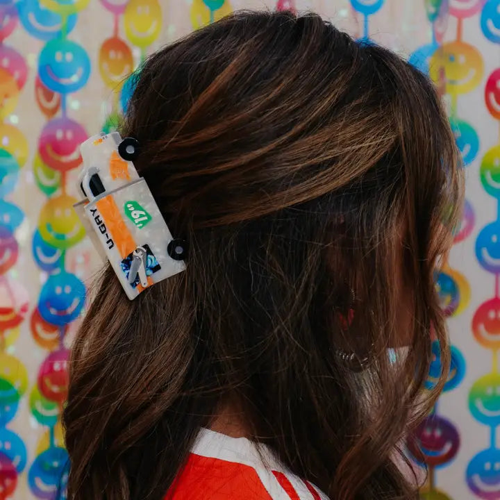 Person with the moving truck shaped hair claw in front of a colorful background with smiley faces.