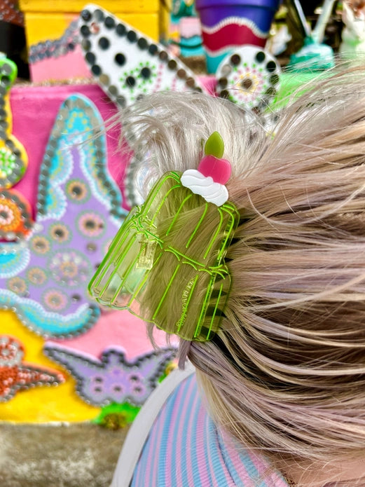 Transparent green jello cake hair claw in blonde hair against a colorful background.