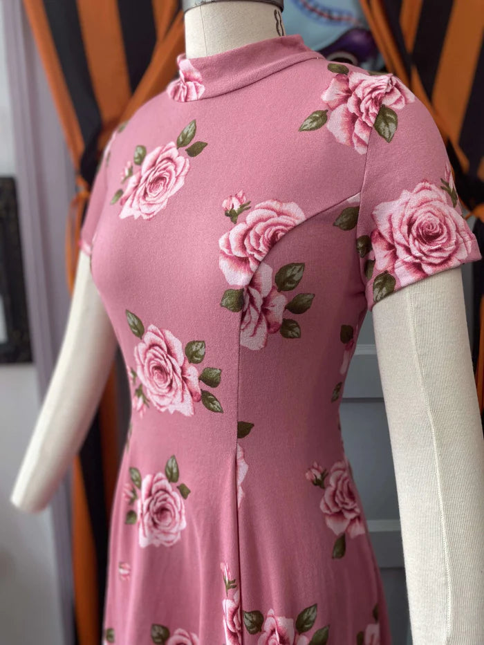 Dress is on a white mannequin. Dress is a dusty rose pink with light pink roses. This photo shows a closer look at the dress to showcase the detail of the roses