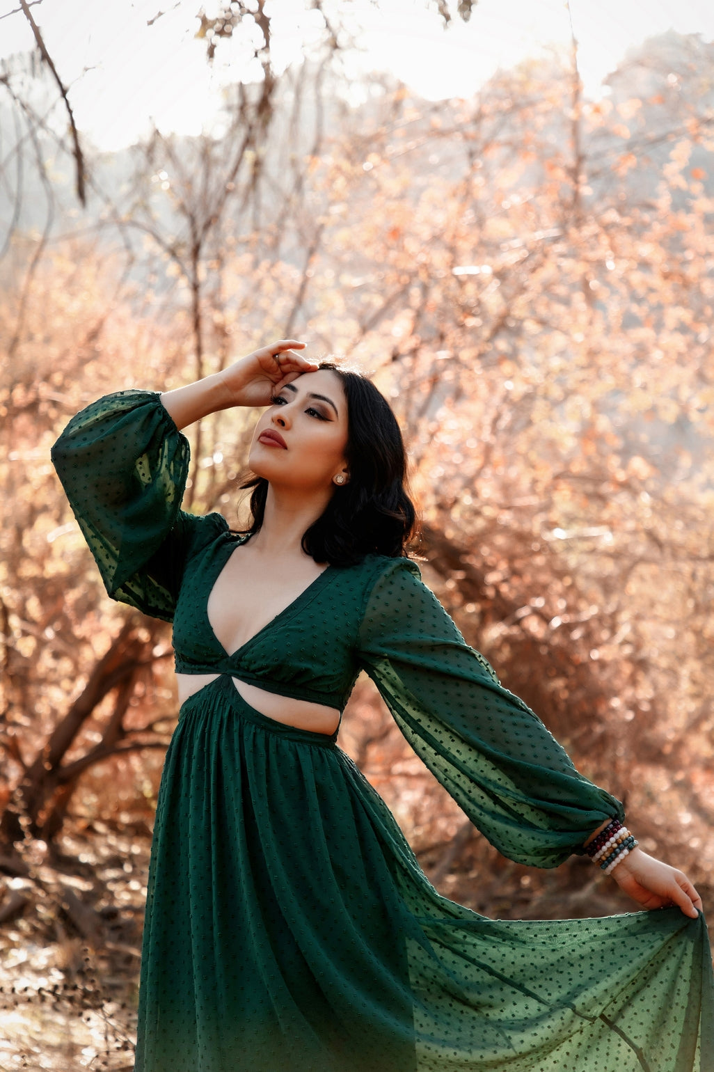 Female presenting model in the green  Feralune dress standing in a forest with autumn foliage.