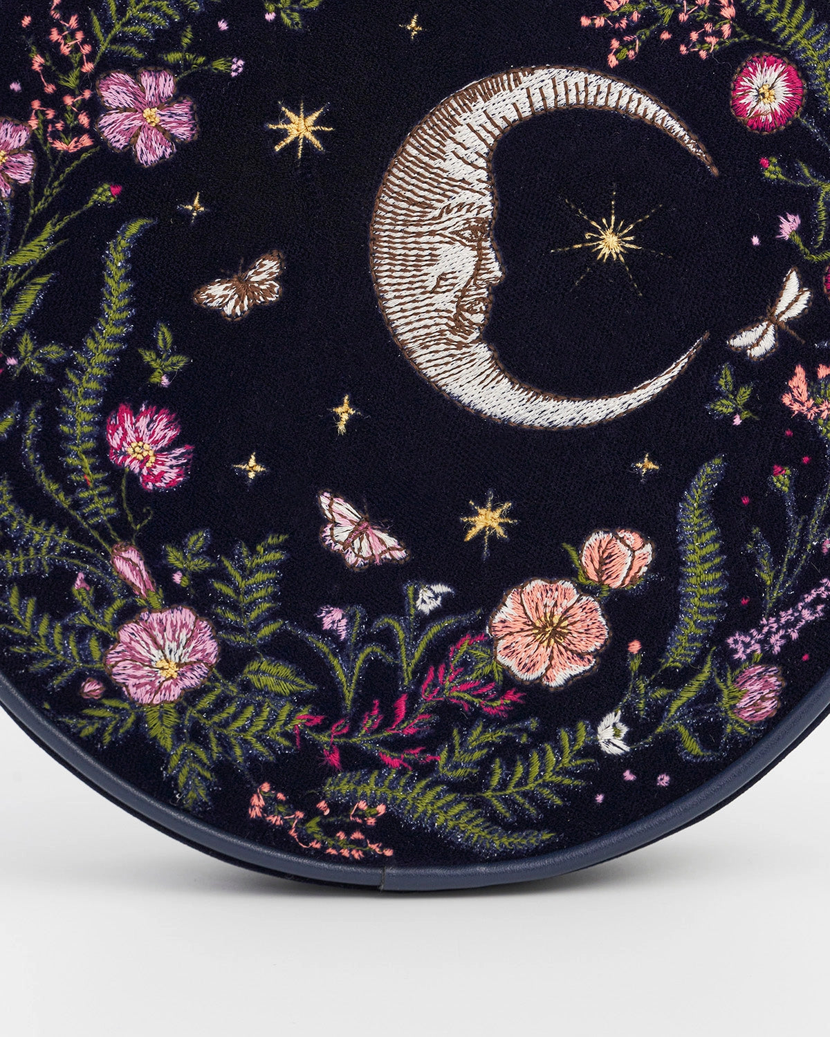 Close up of the moon and floral embroidery on the front of the purse against a white background.