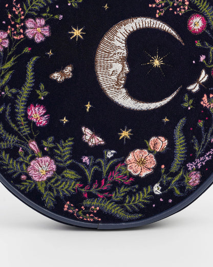 Close up of the moon and floral embroidery on the front of the purse against a white background.