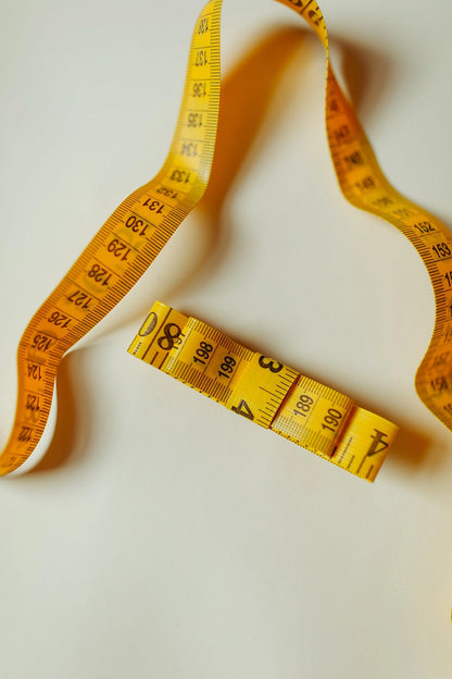 Classic yellow measuring tape bow next to a non-bow measuring tape against a cream background.