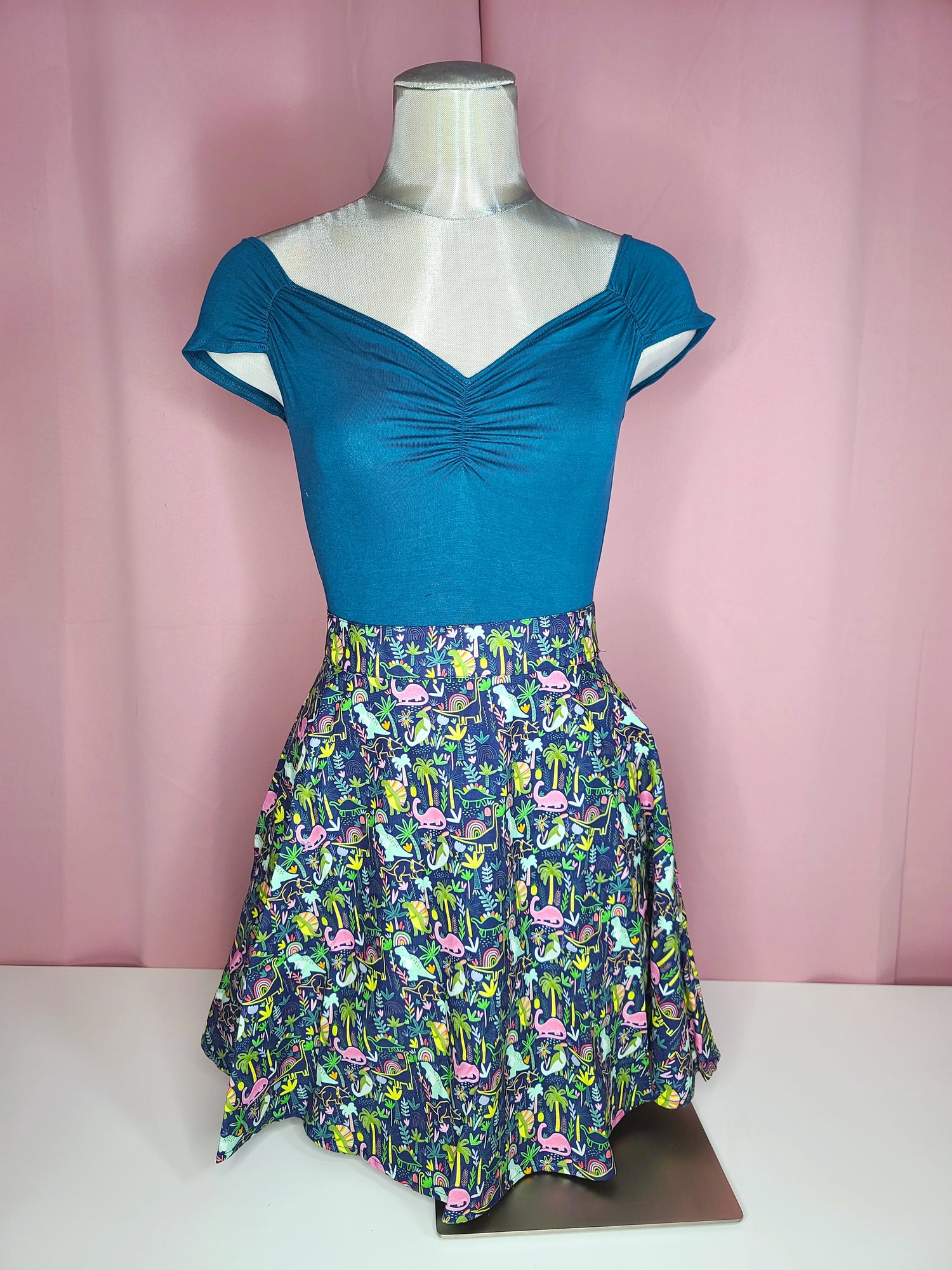 Top on mannequin with skirt against a pink background 