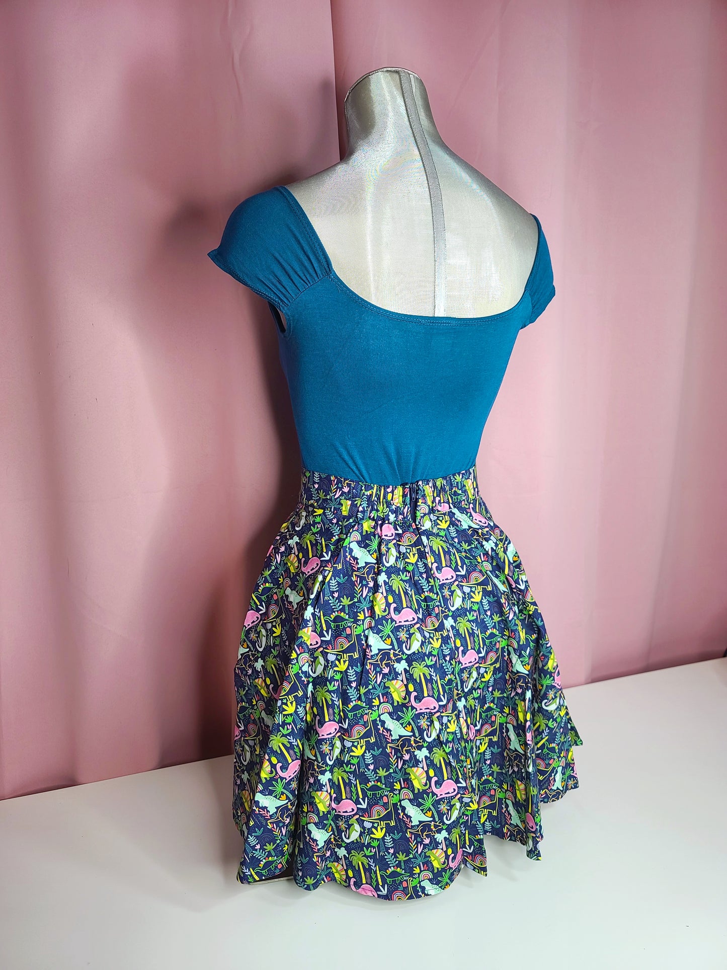 Back of the top on mannequin with a skirt against a pink background at an angle