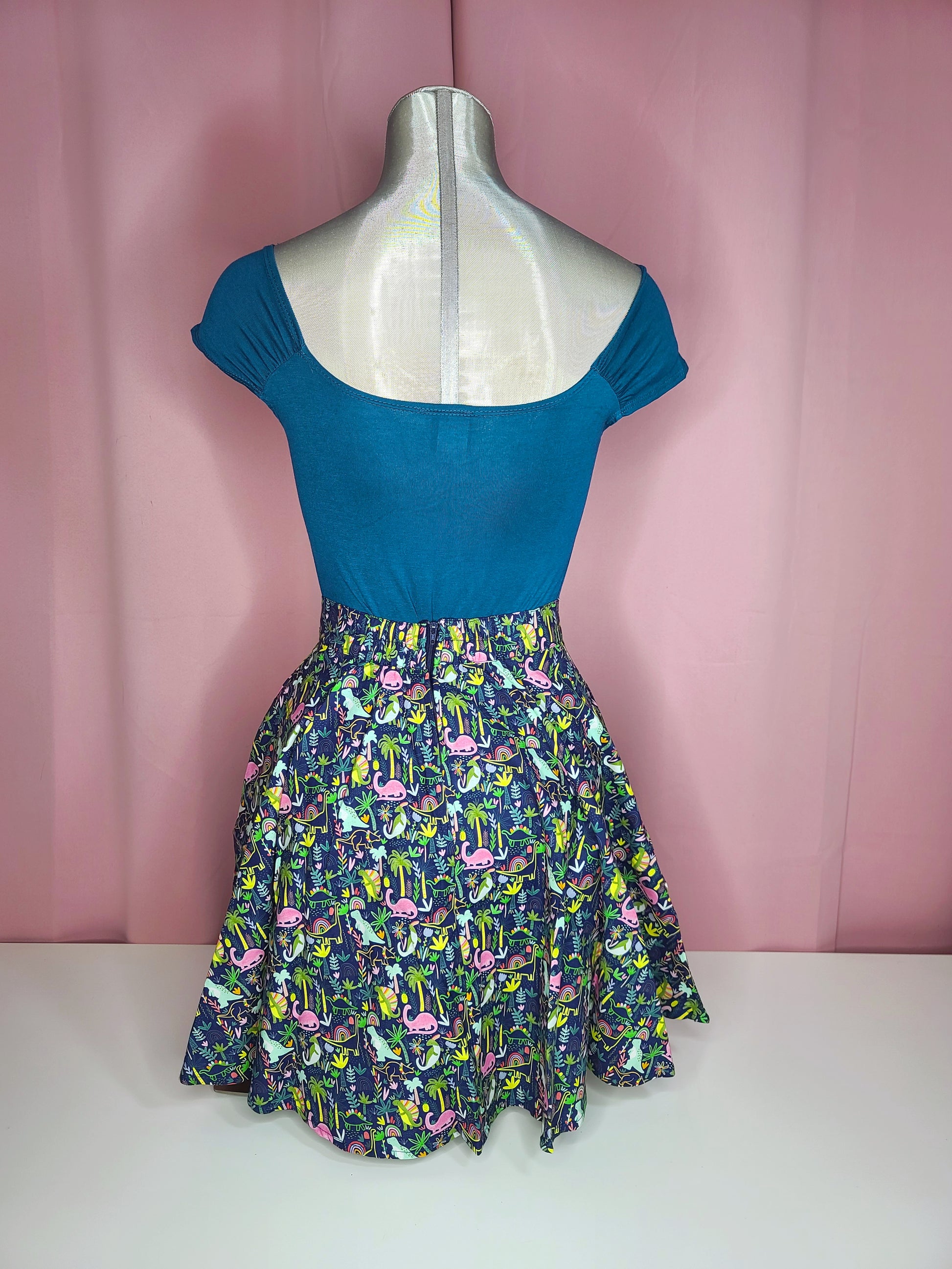 Back of the top on mannequin with a skirt against a pink background 