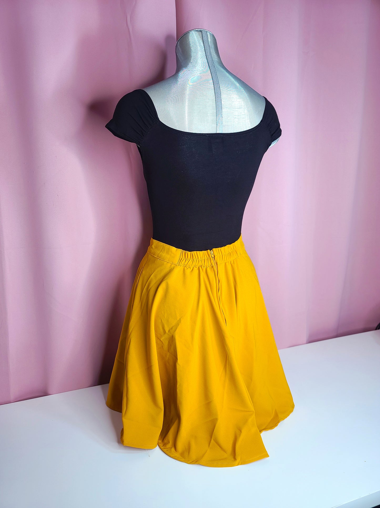 Back of the top on mannequin with a skirt against a pink background 