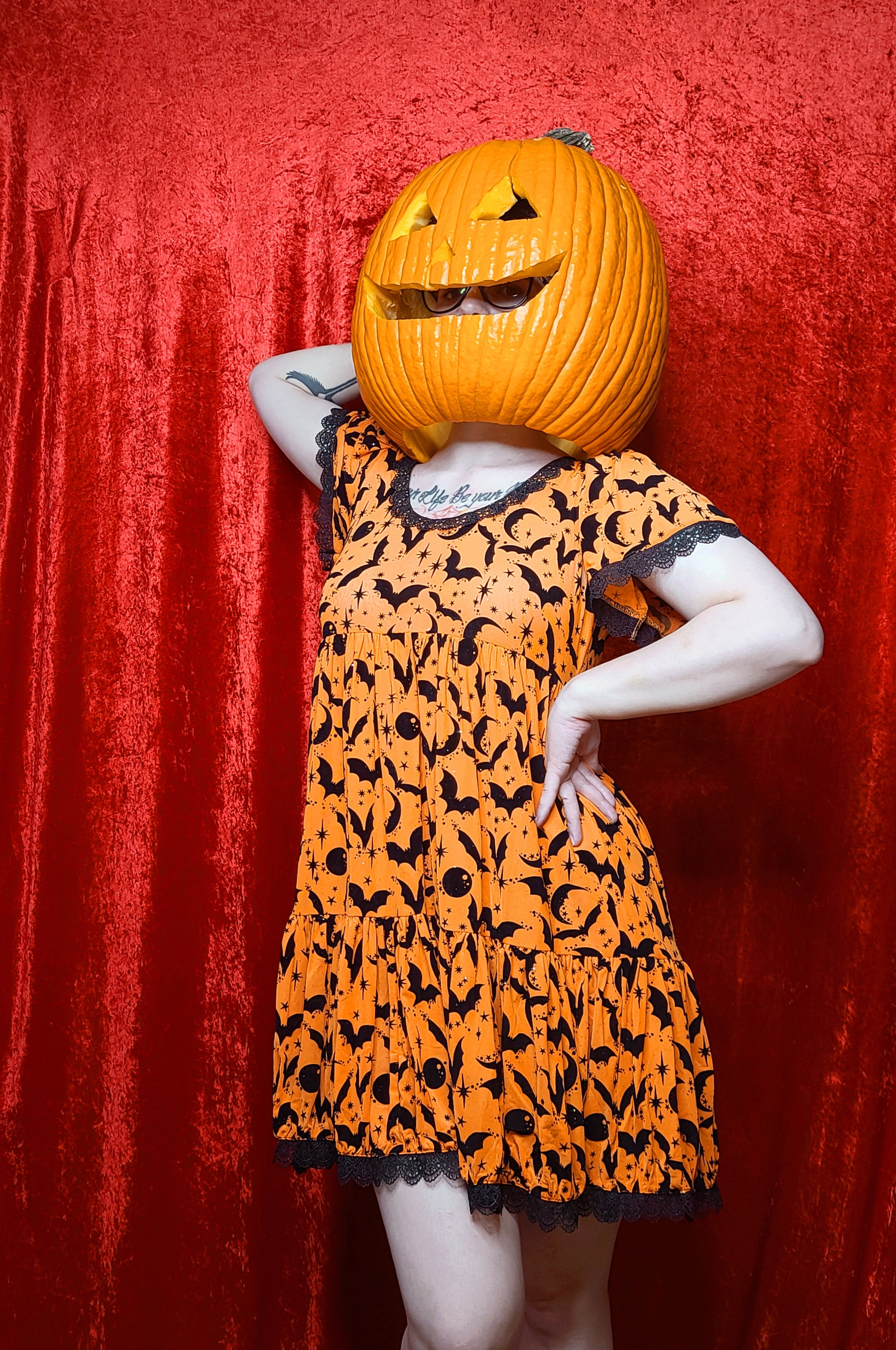 Model wearing a jack o lantern head showcasing dress against a red background