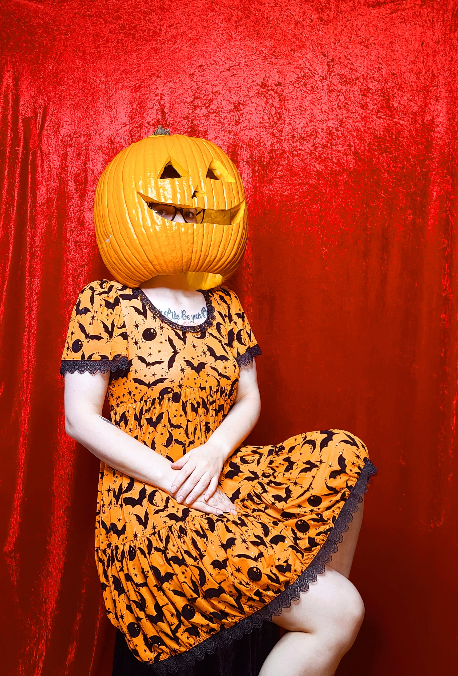 Model wearing a jack o lantern head showcasing dress against a red background