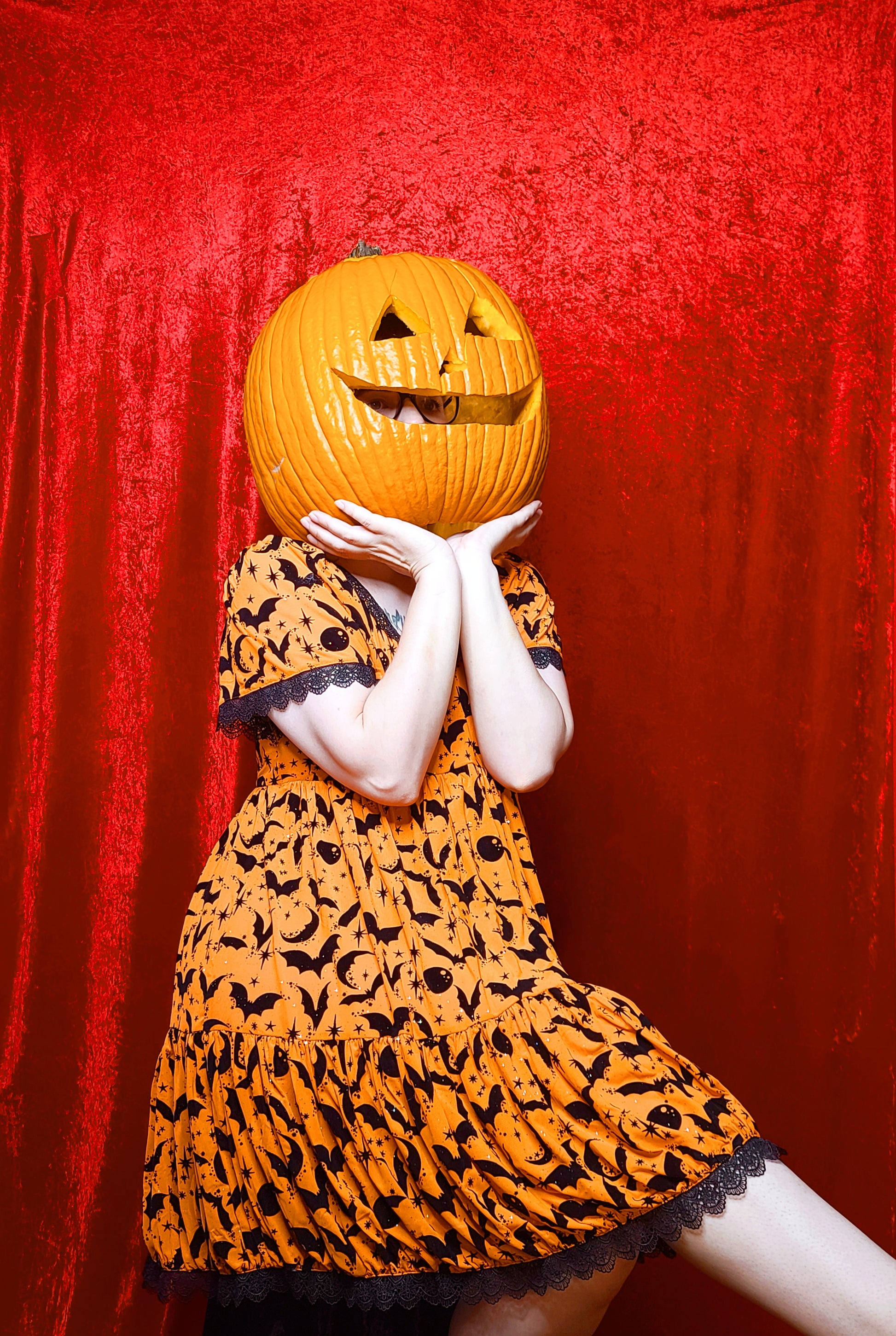 Model wearing a jack o lantern head showcasing dress against a red background