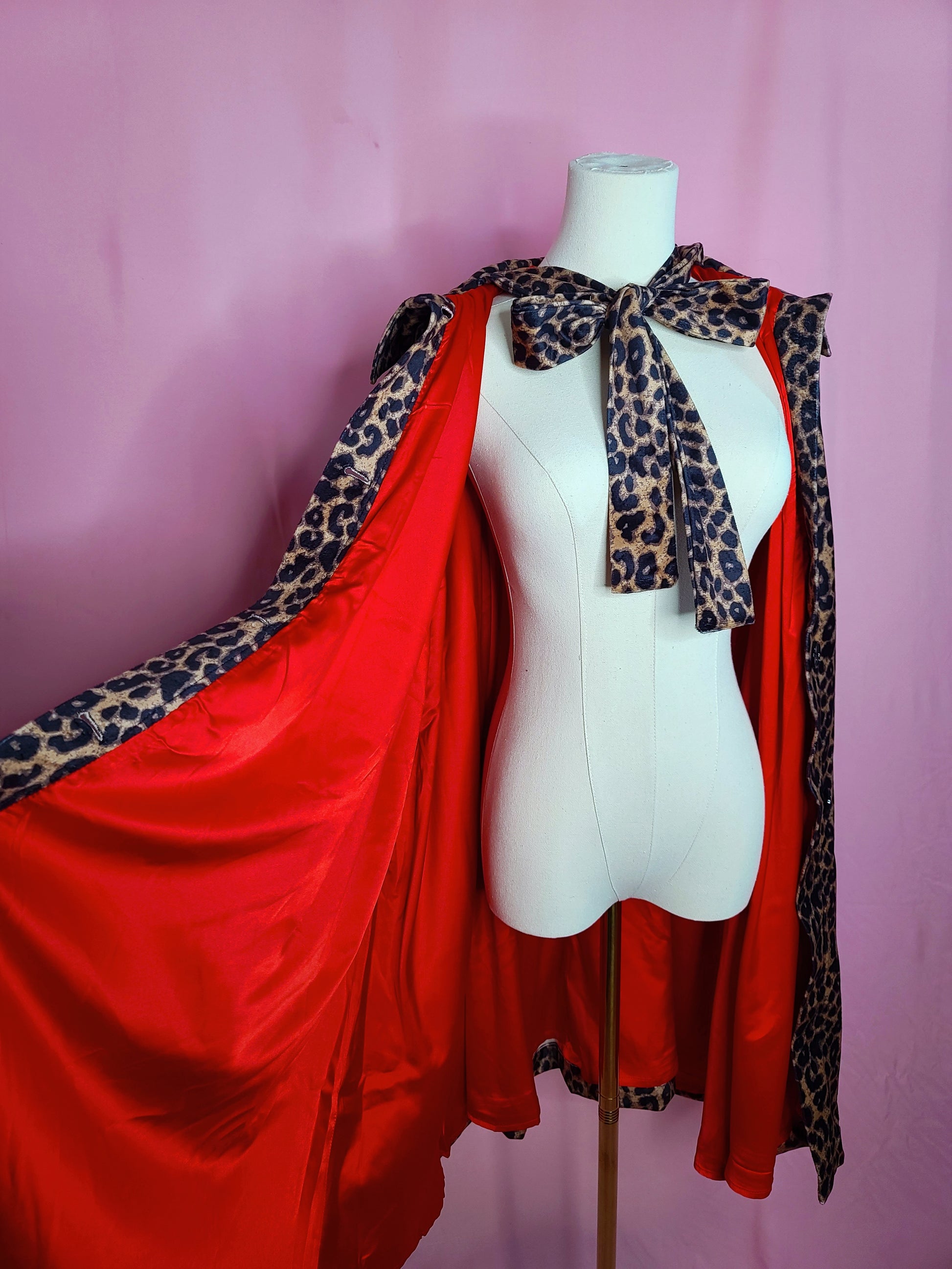 Cape on mannequin showcasing the red fabric on the inside of the cape. Against a pink background