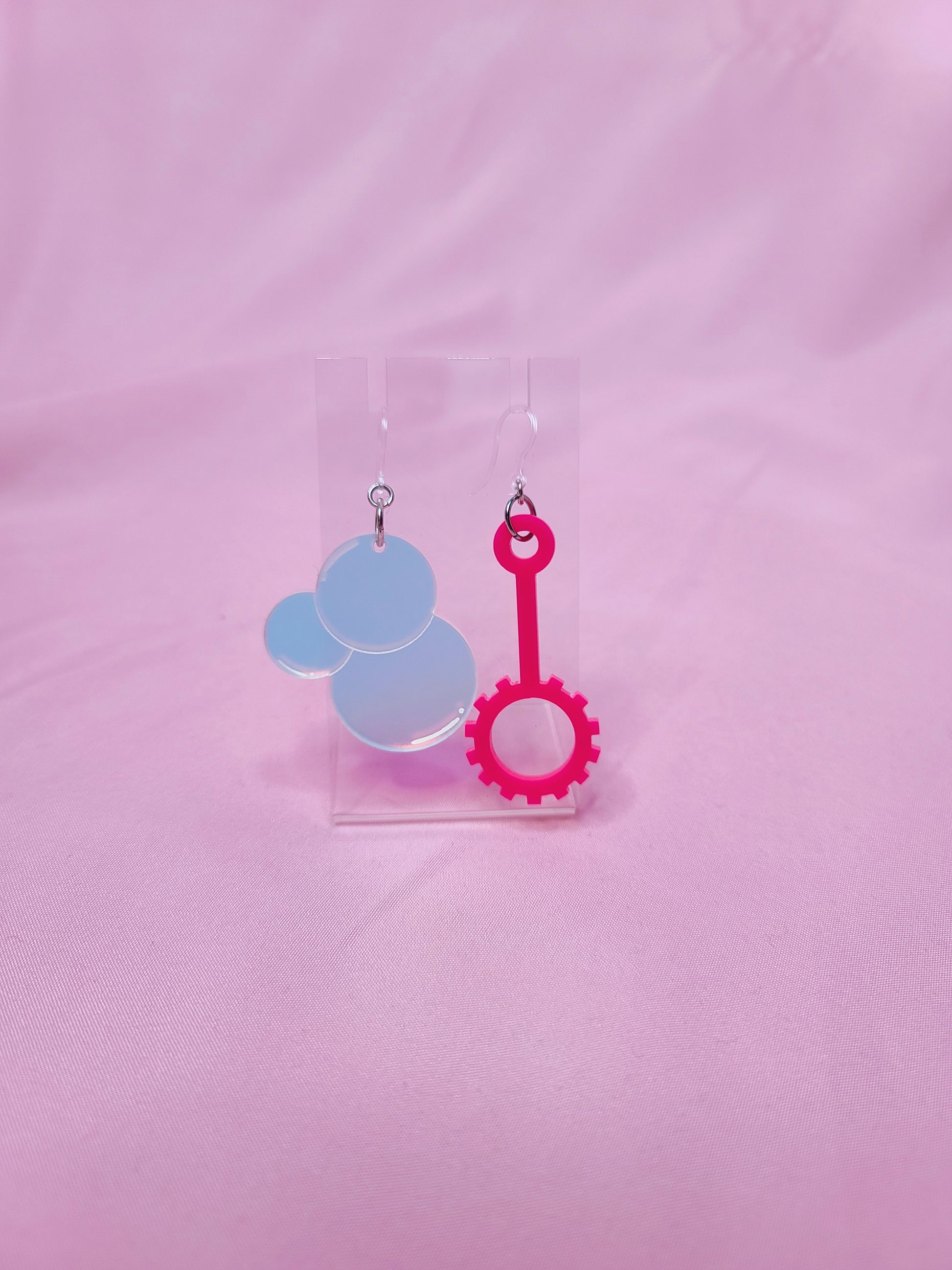 Earrings on a clear earring display against a pink background