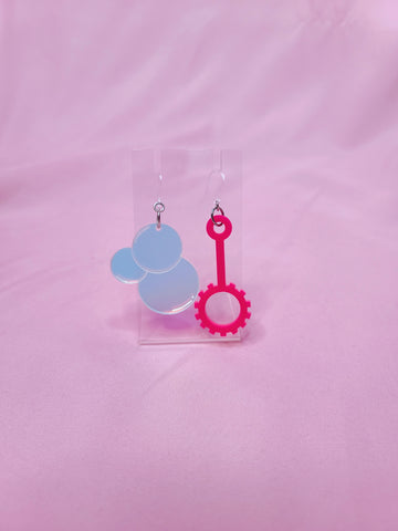 Earrings on a clear earring display against a pink background
