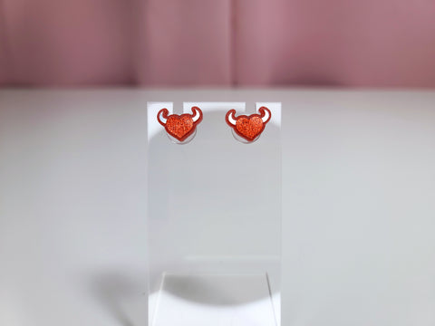 Earrings on a clear earring display against a pink and white background