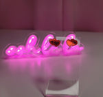 Earrings on a clear display with a pink neon sign behind out of focus saying "oh la la"
