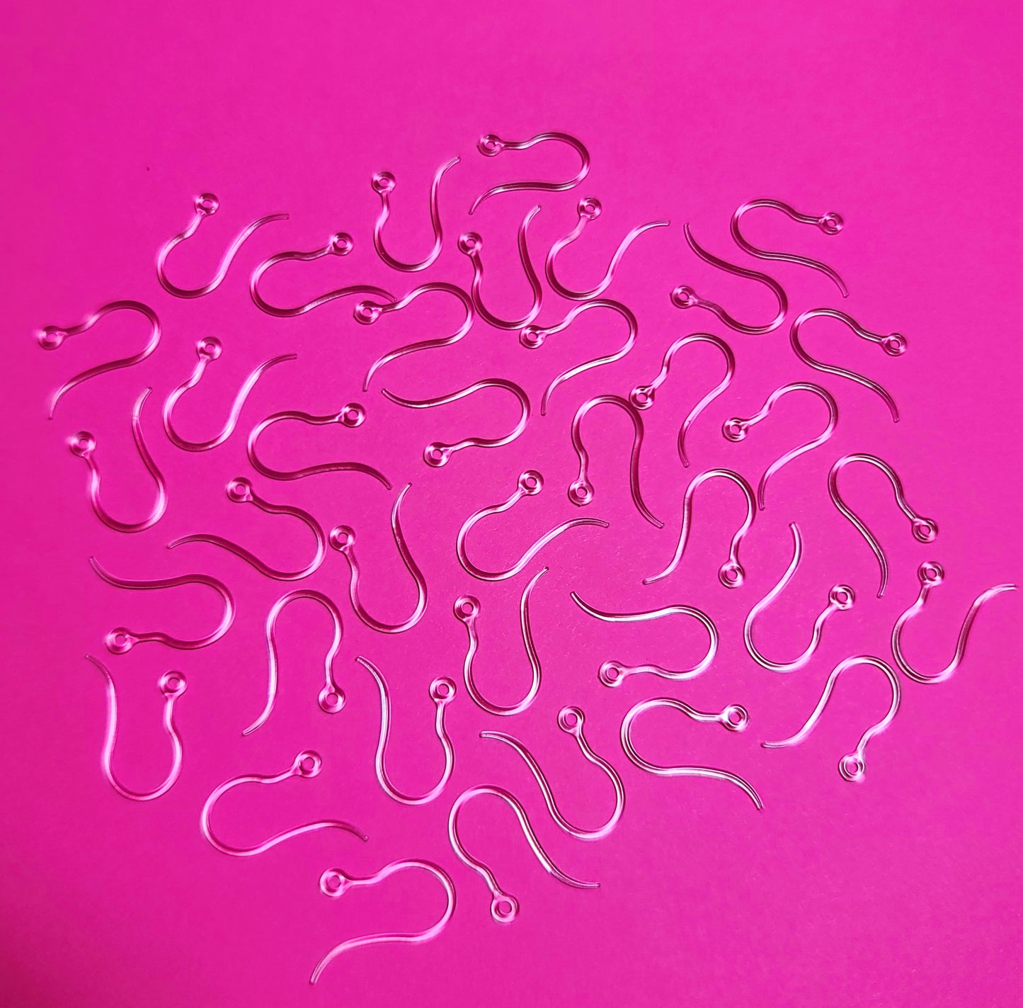 A group of plastic earrings hooks against a dark pink background