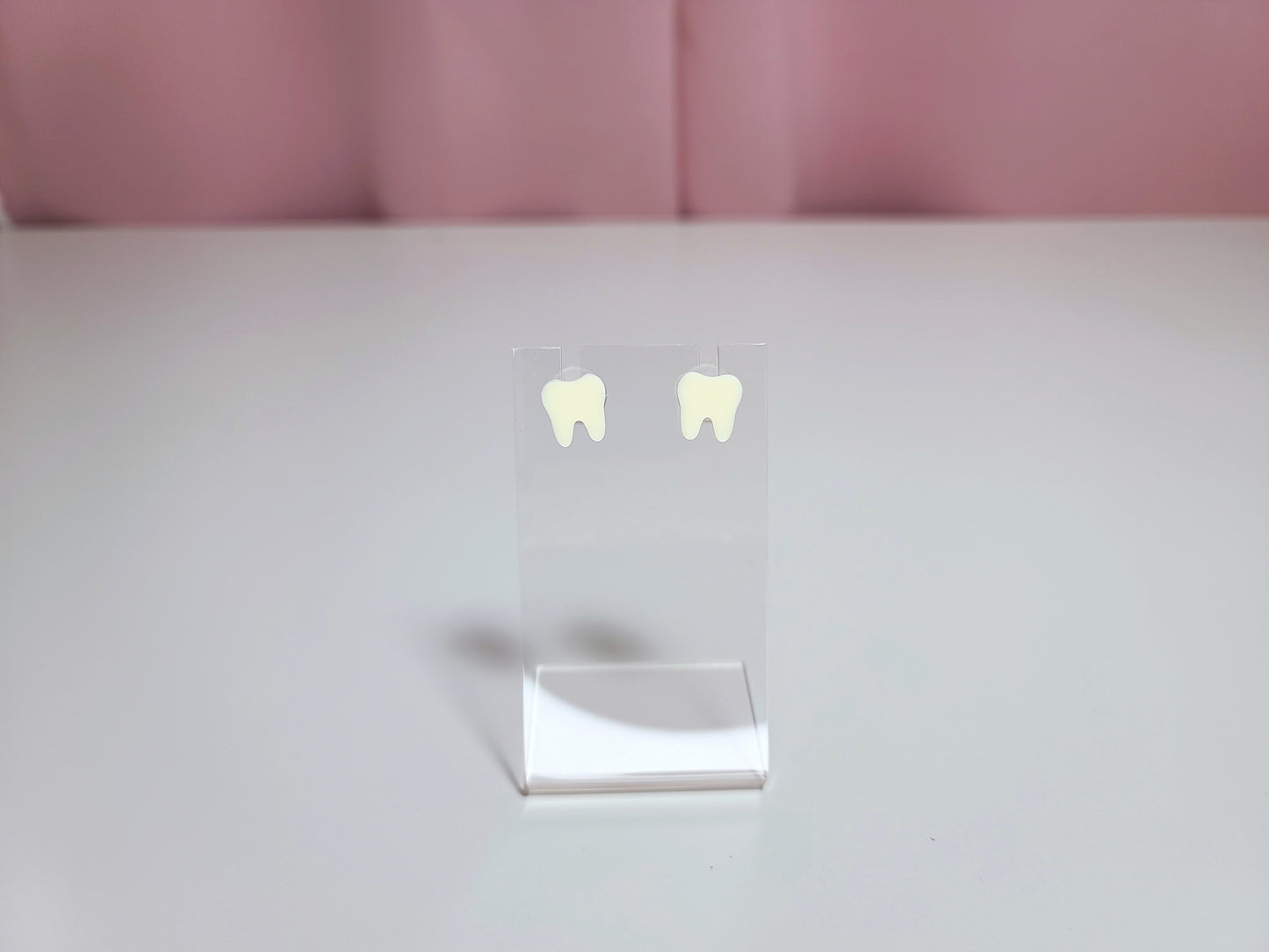 Earrings on a clear display against a pink and white background