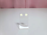 Earrings on a clear display against a pink and white background