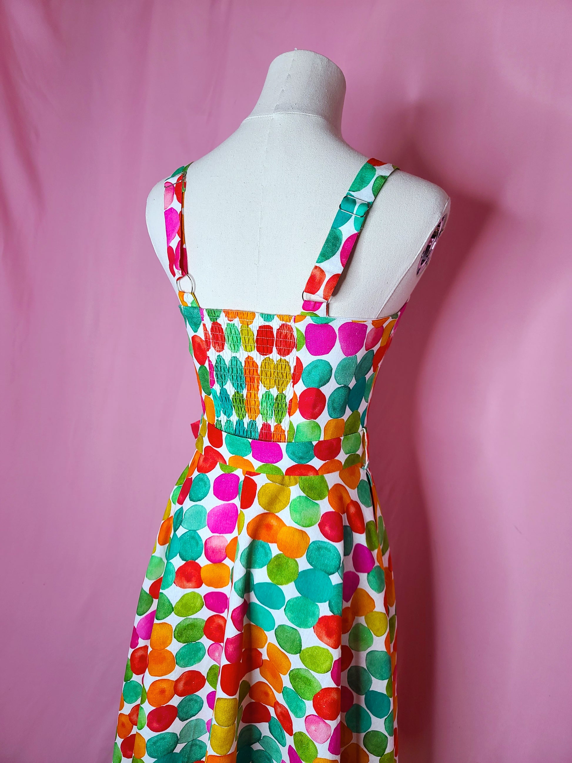 Close up of the back of the dress showing the elastic ruched back, and the adjustable straps against a pink background