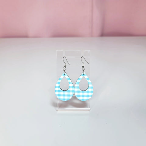 Earrings on a clear display against a white and pink background 