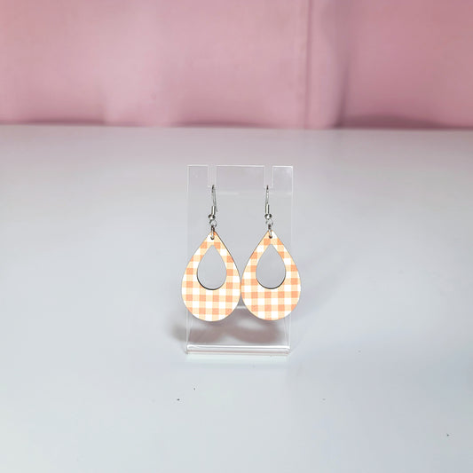 Earrings on a clear display against a white and pink background