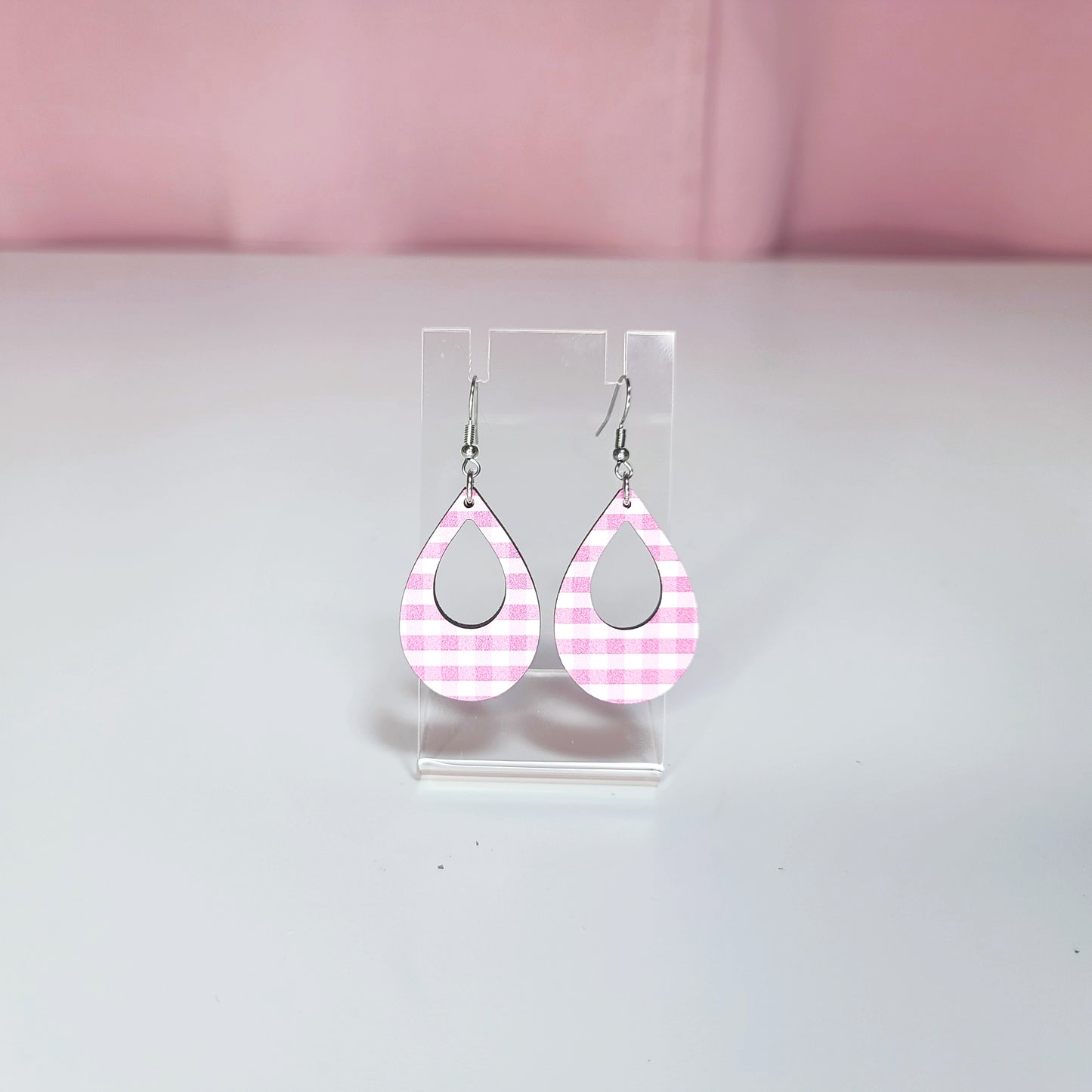 Earrings on a clear display against a white and pink background