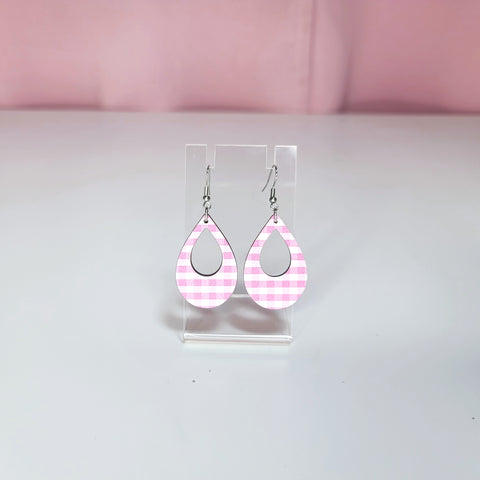 Earrings on a clear display against a white and pink background