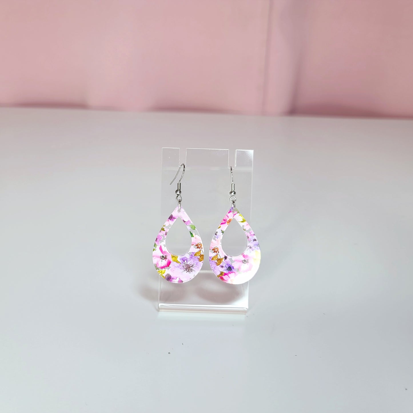 Earrings on a clear display against a white and pink background