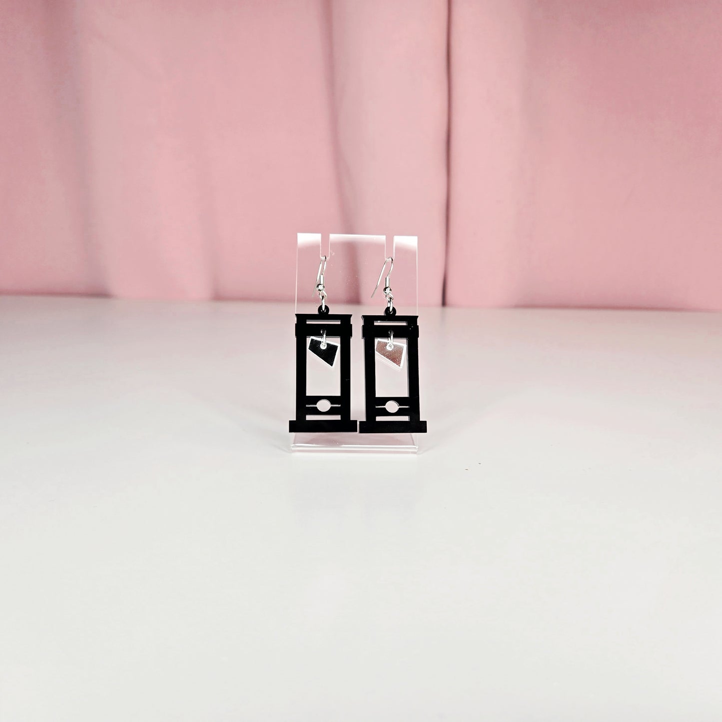 Earrings on a clear earring display against a pink and white background.