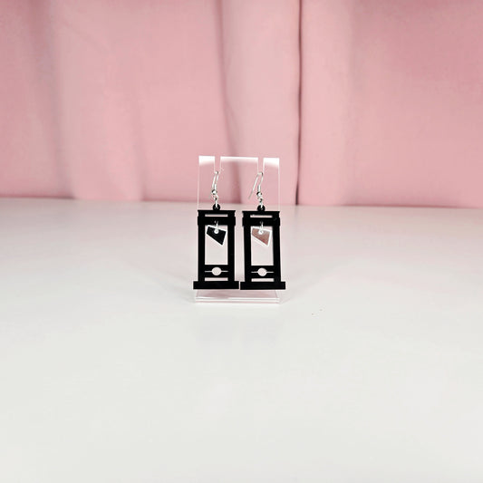 Earrings on a clear earring display against a pink and white background.