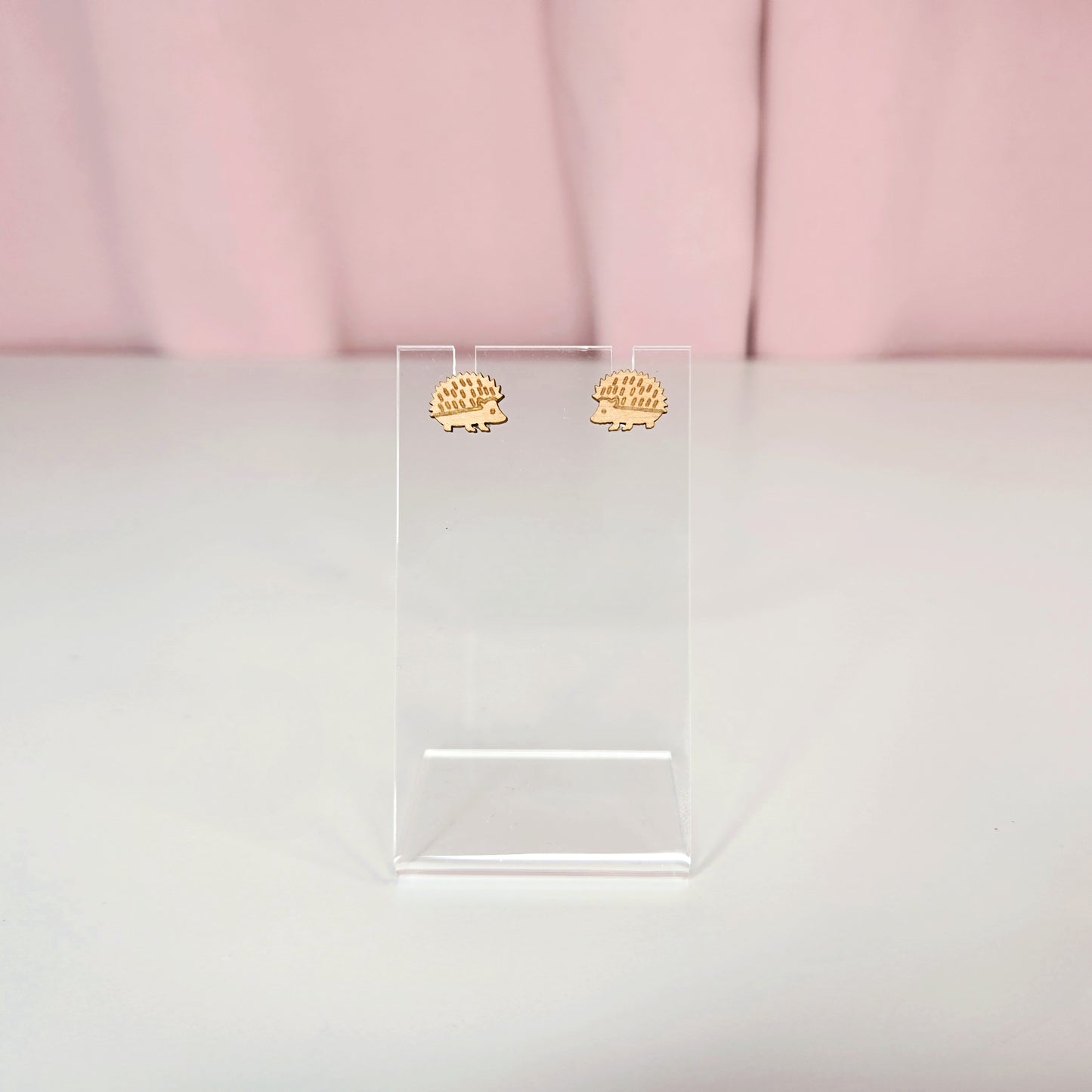 Stud earrings on a clear earring display against a pink and white background.