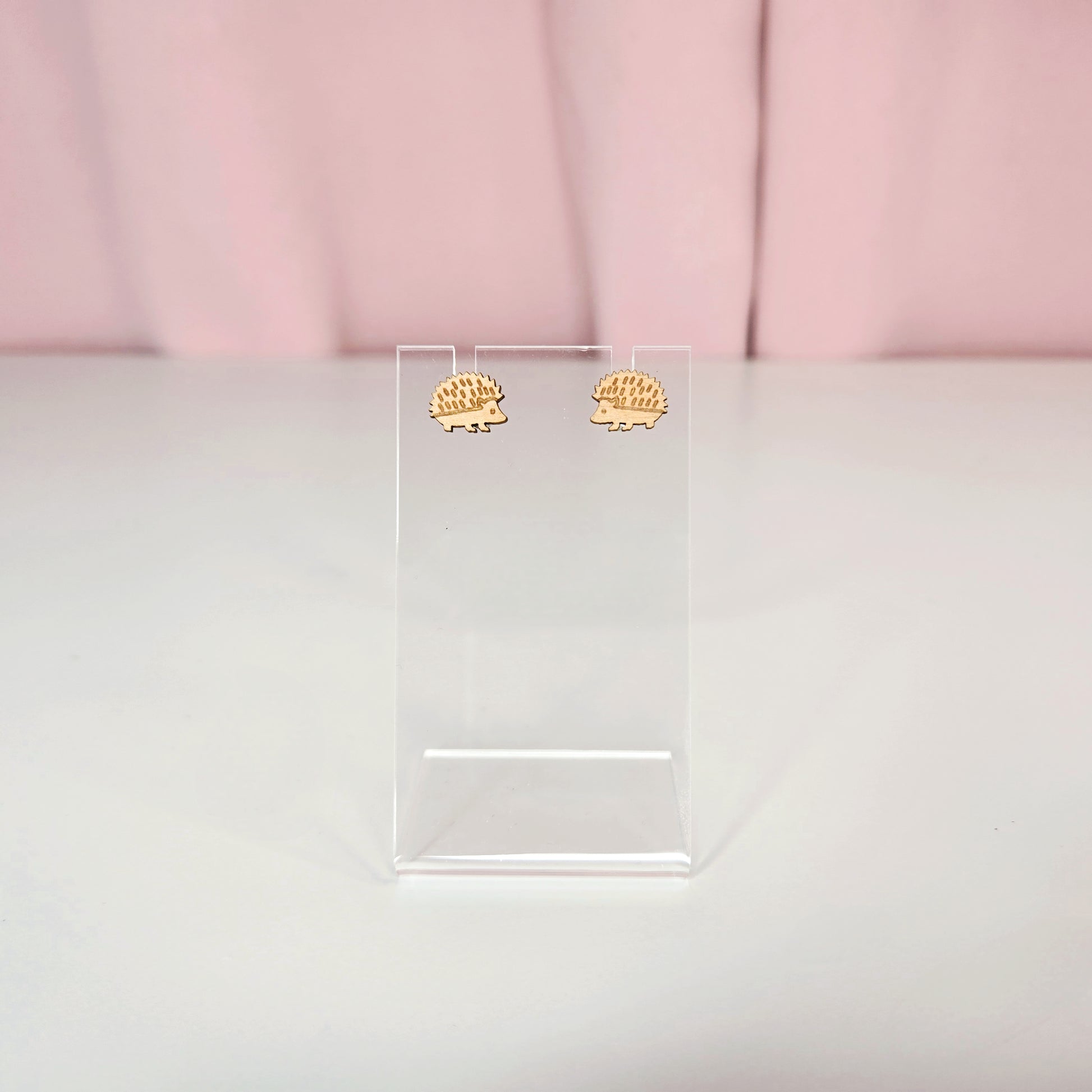 Stud earrings on a clear earring display against a pink and white background.