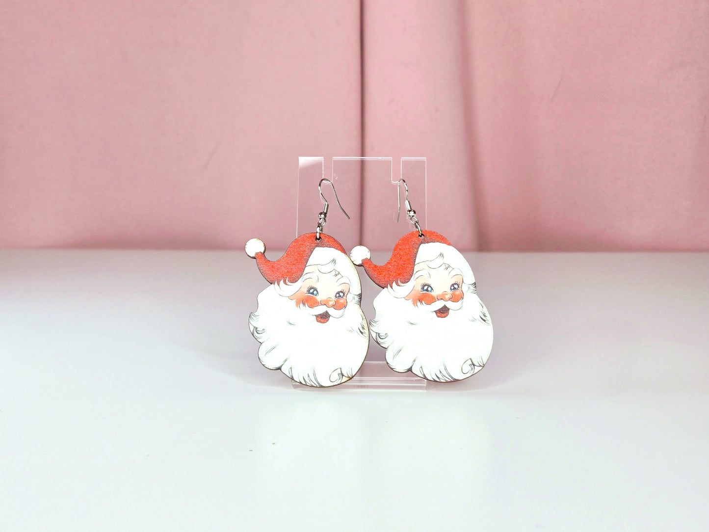 A vintage styled White Santa head with red hat and white beard on a clear earring display against a white and pikc background