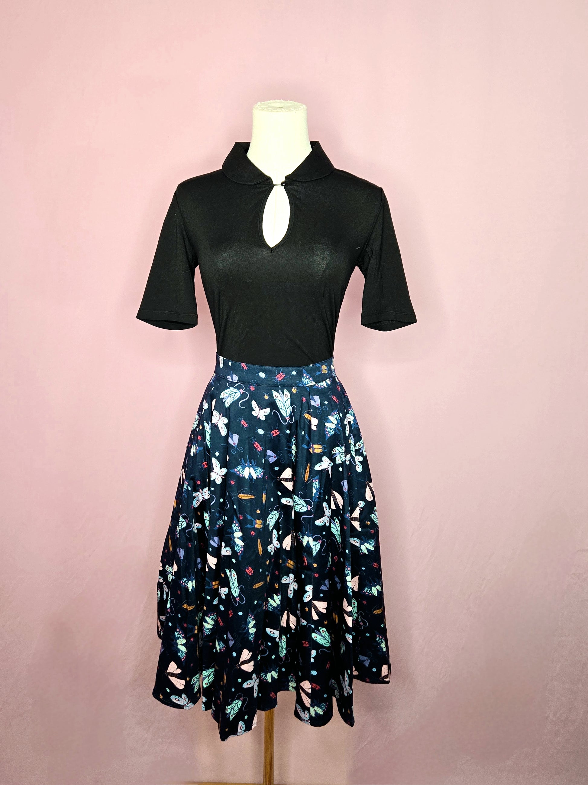 Skirt paired with the Keynote Blouse in Black on a white mannequin against a pink background