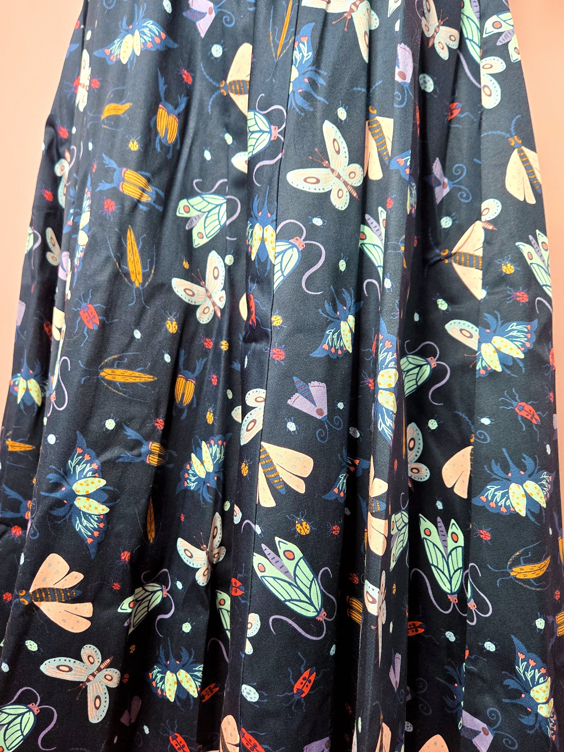 Close up of the different pastel colored moths and beetles on the navy background of the skirt. Skirt shown against a pink background