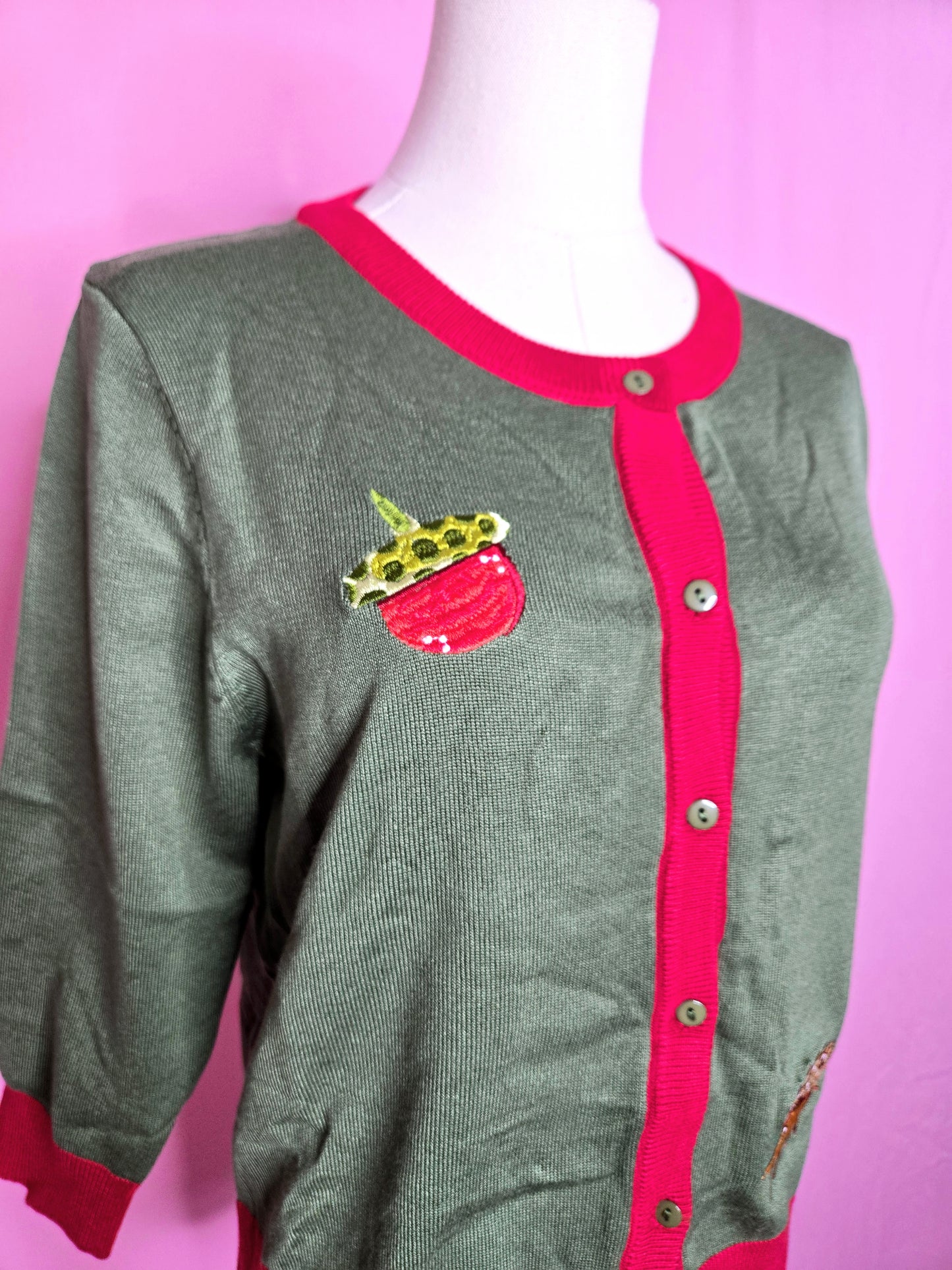 Close up of the acorn on the top of the cardigan against a pink background