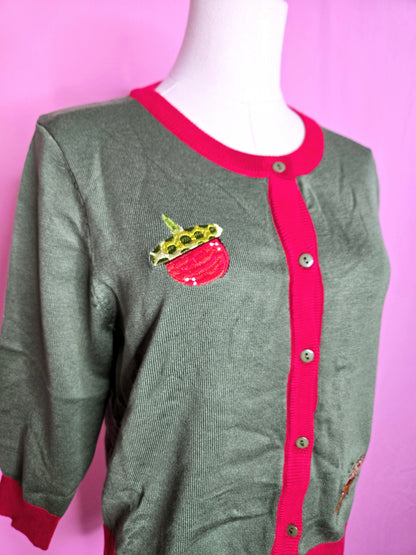 Close up of the acorn on the top of the cardigan against a pink background